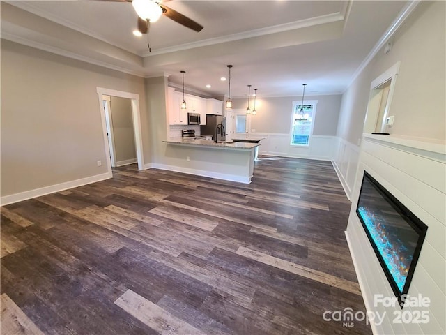 unfurnished living room with a raised ceiling, ceiling fan, crown molding, and dark hardwood / wood-style floors