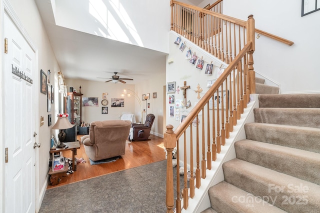 stairs featuring ceiling fan, a high ceiling, baseboards, and wood finished floors