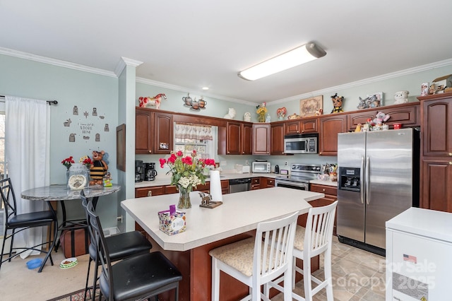 kitchen featuring a breakfast bar, a center island, crown molding, light countertops, and appliances with stainless steel finishes