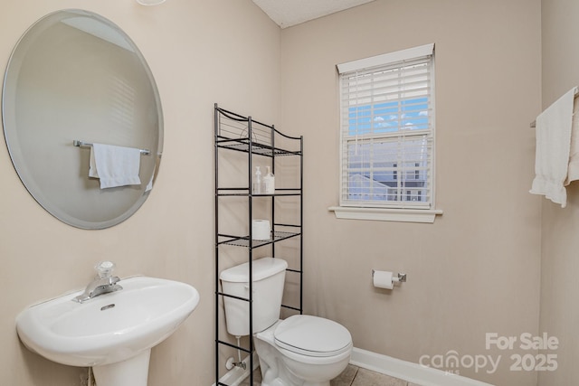 half bath with tile patterned flooring, a sink, toilet, and baseboards