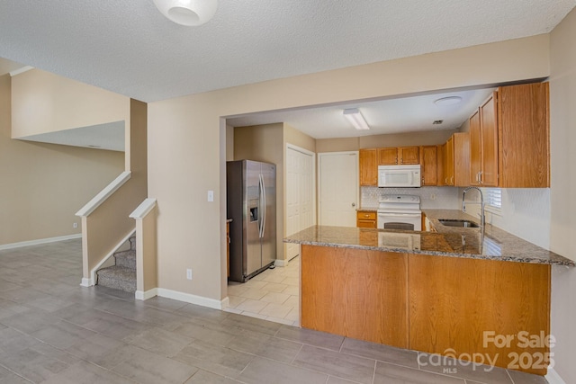 kitchen with brown cabinets, stone countertops, a sink, white appliances, and a peninsula