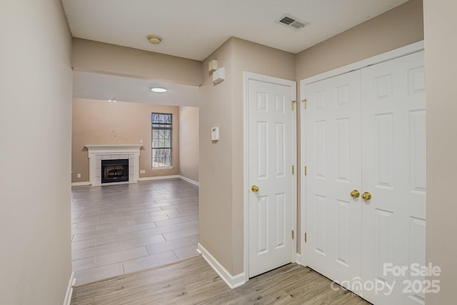 entryway featuring light wood finished floors, a fireplace, visible vents, and baseboards