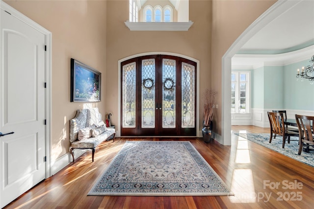 entryway with arched walkways, a wainscoted wall, dark wood-style flooring, french doors, and a chandelier