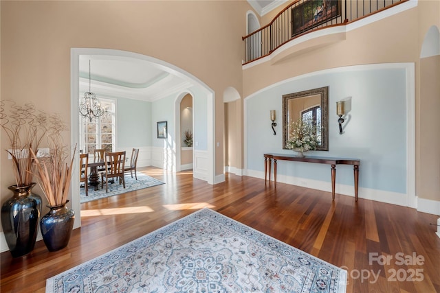 entrance foyer featuring a high ceiling, wood finished floors, ornamental molding, a tray ceiling, and an inviting chandelier