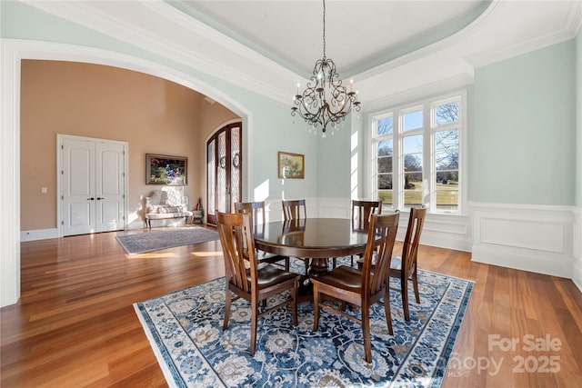 dining room featuring arched walkways, a raised ceiling, and wood finished floors