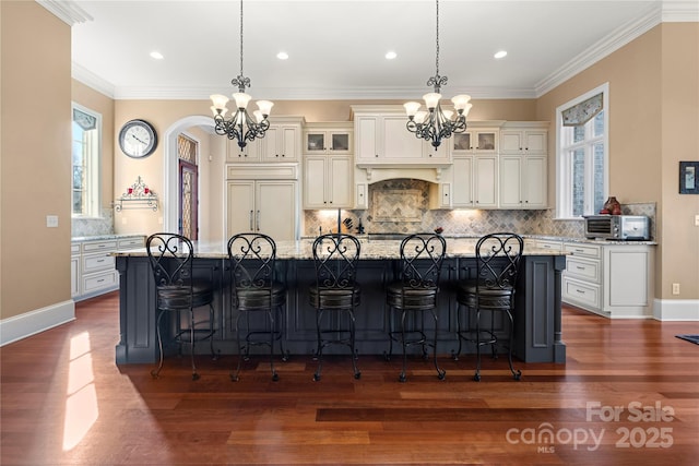 kitchen featuring an island with sink, an inviting chandelier, glass insert cabinets, and light stone countertops