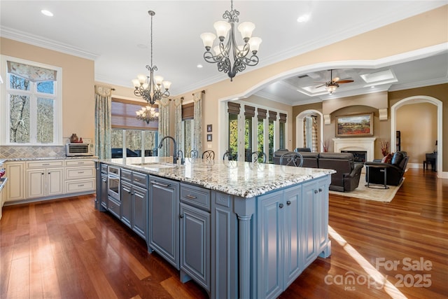 kitchen featuring a fireplace, open floor plan, a kitchen island with sink, a sink, and blue cabinets