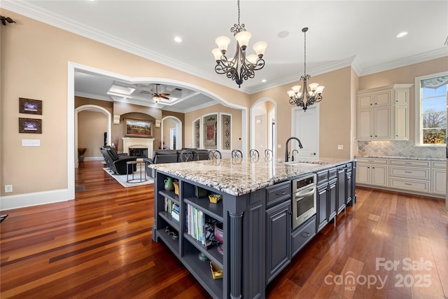 kitchen featuring oven, a sink, open floor plan, light stone countertops, and an island with sink