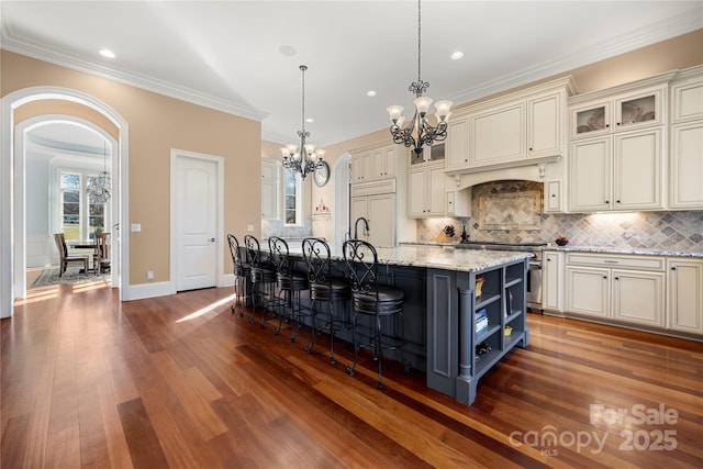 kitchen featuring light stone counters, a center island with sink, open shelves, glass insert cabinets, and pendant lighting