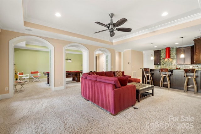 living room featuring arched walkways, ornamental molding, and a raised ceiling