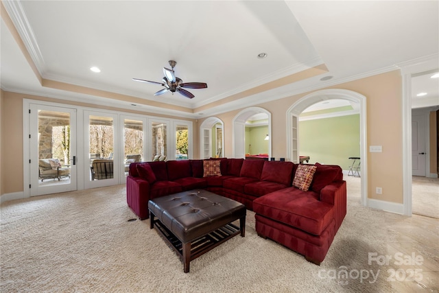 living area with a tray ceiling, light colored carpet, crown molding, and arched walkways