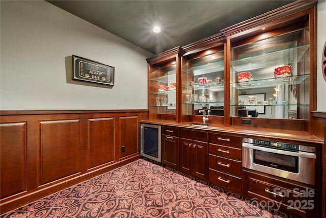 bar with a wainscoted wall, stainless steel oven, a sink, wet bar, and beverage cooler