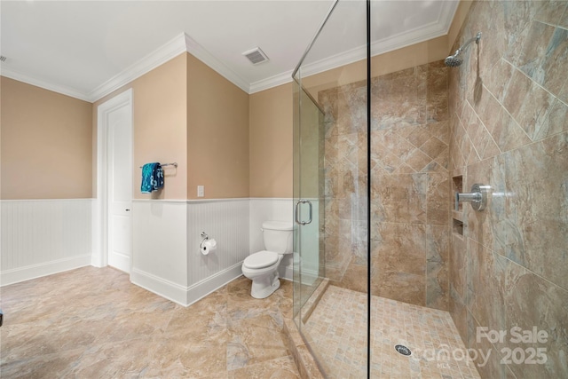 bathroom with toilet, a wainscoted wall, visible vents, ornamental molding, and a stall shower