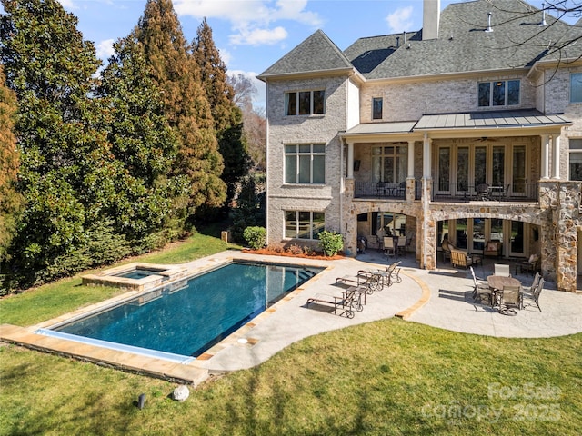 rear view of property with a shingled roof, a balcony, a chimney, a yard, and a patio area