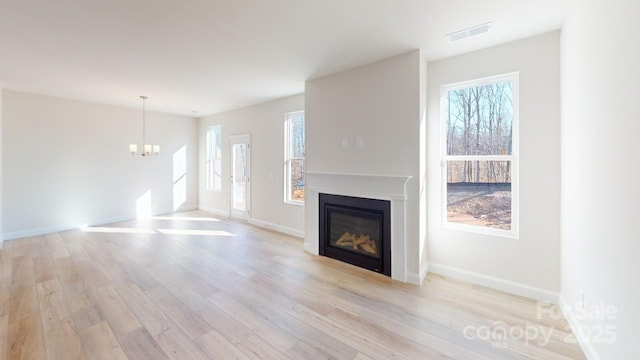 unfurnished living room with a notable chandelier, plenty of natural light, and light hardwood / wood-style flooring