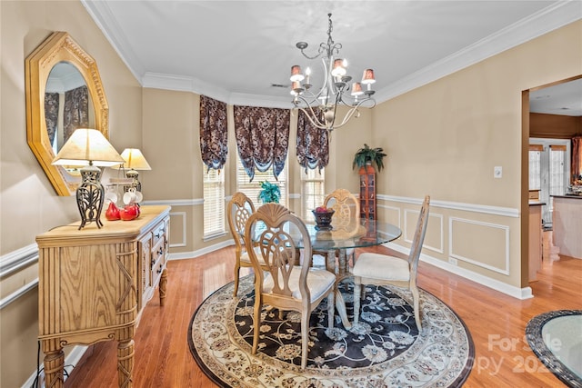 dining area with a wainscoted wall, a decorative wall, an inviting chandelier, ornamental molding, and light wood-type flooring