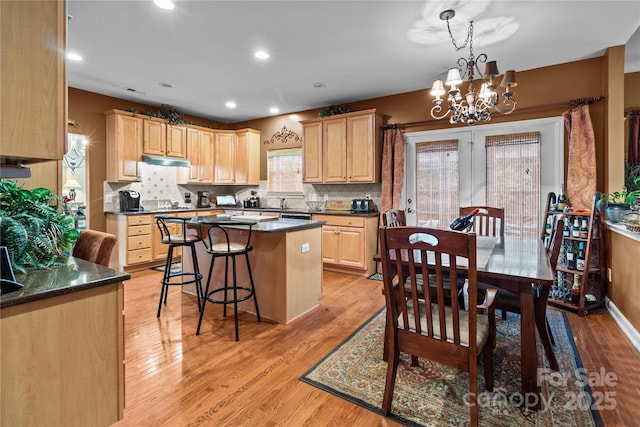 kitchen with dark countertops, light brown cabinets, a kitchen island, and light wood-style flooring