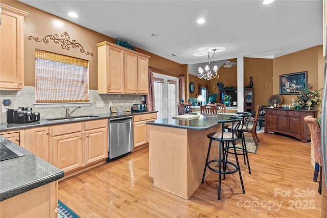 kitchen with dark countertops, a breakfast bar area, a sink, light brown cabinets, and stainless steel dishwasher