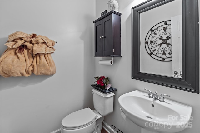 half bathroom featuring a sink, toilet, and baseboards