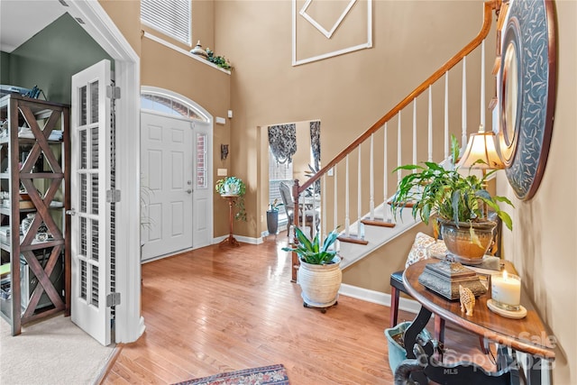 entryway featuring a towering ceiling, stairway, baseboards, and wood finished floors