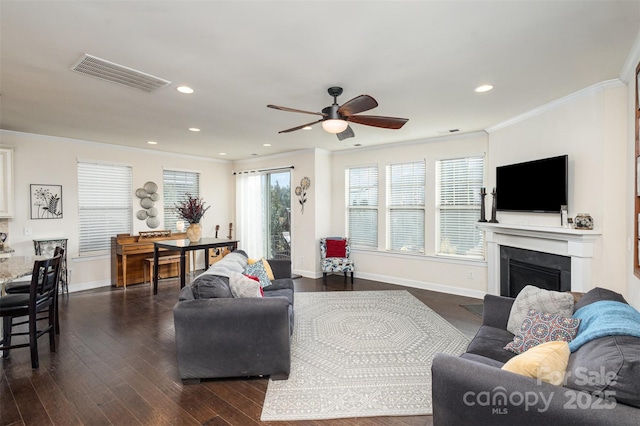 living area featuring baseboards, visible vents, a fireplace with flush hearth, dark wood-type flooring, and crown molding