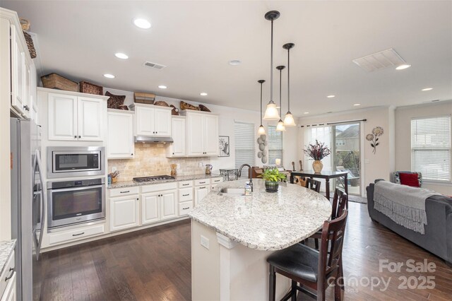 kitchen with a breakfast bar area, stainless steel appliances, a sink, dark wood-style floors, and tasteful backsplash