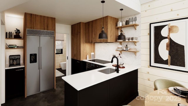 kitchen with sink, wood walls, stainless steel built in refrigerator, and decorative light fixtures