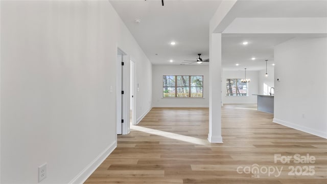 interior space featuring ceiling fan with notable chandelier, baseboards, recessed lighting, and light wood-type flooring