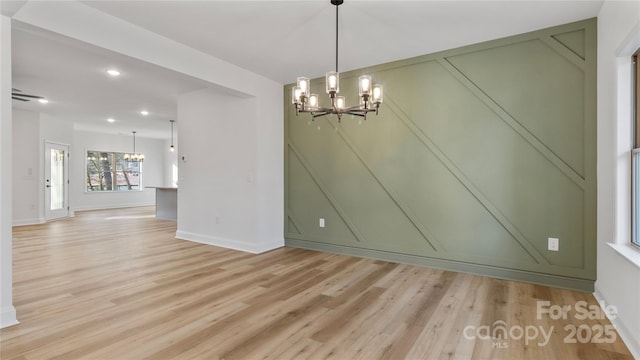 unfurnished dining area with a notable chandelier, baseboards, recessed lighting, and light wood finished floors