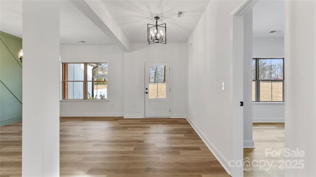 entrance foyer featuring light wood finished floors, baseboards, a notable chandelier, and visible vents