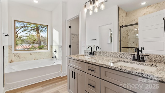 full bathroom with a spacious closet, a bath, wood finished floors, and a sink