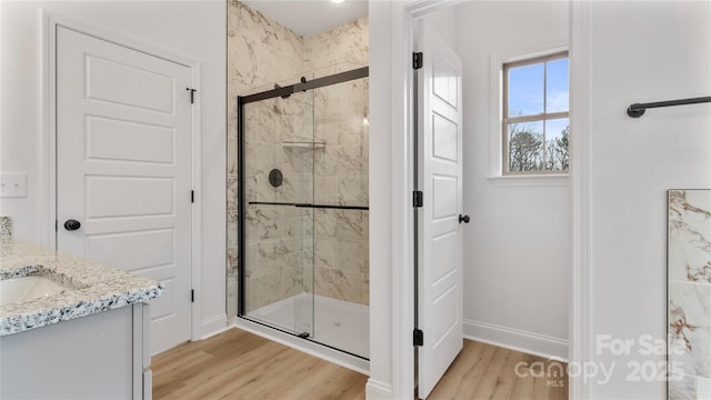 full bathroom featuring vanity, baseboards, wood finished floors, and a stall shower