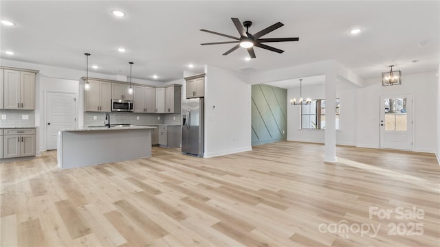 kitchen with open floor plan, hanging light fixtures, an island with sink, gray cabinets, and stainless steel appliances