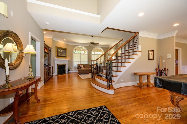 entryway featuring ornamental molding, a fireplace with flush hearth, wood finished floors, baseboards, and stairs