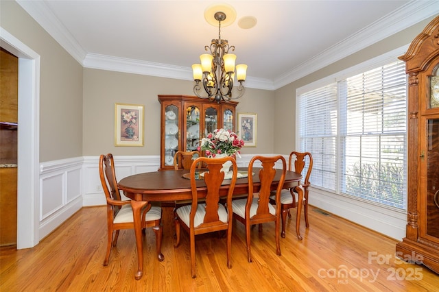 dining area with a notable chandelier, a wainscoted wall, visible vents, light wood-style floors, and ornamental molding