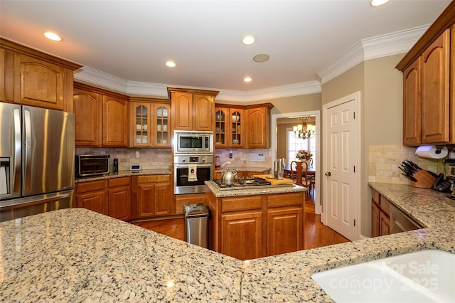 kitchen featuring appliances with stainless steel finishes, brown cabinets, glass insert cabinets, and light stone countertops