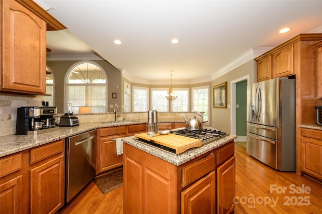 kitchen featuring light wood-style flooring, ornamental molding, a center island, stainless steel appliances, and a sink