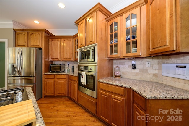 kitchen with stainless steel appliances, ornamental molding, glass insert cabinets, and light stone countertops