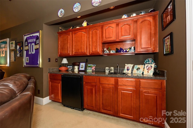 kitchen featuring dark stone countertops, a sink, baseboards, and fridge