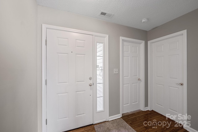 entrance foyer with a textured ceiling, dark wood-style flooring, plenty of natural light, and visible vents