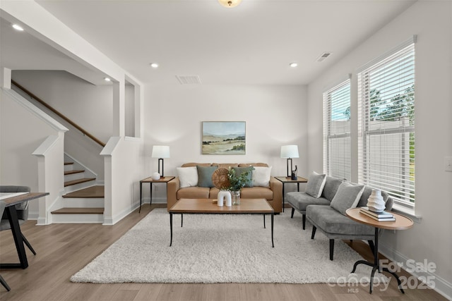 living area featuring stairway, light wood-type flooring, visible vents, and baseboards