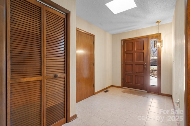 entrance foyer with a textured ceiling, a skylight, light tile patterned flooring, and baseboards