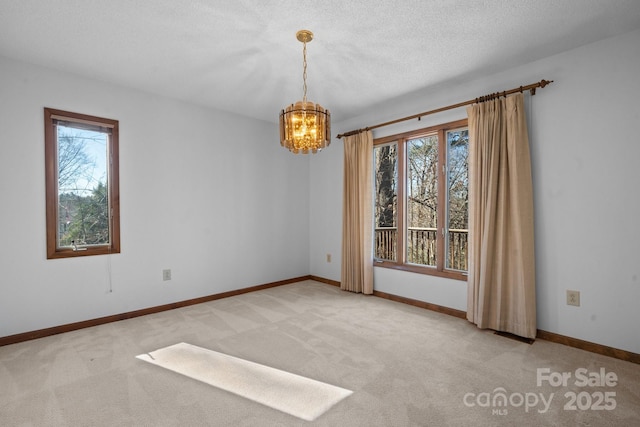 empty room featuring a chandelier, light colored carpet, a textured ceiling, and baseboards