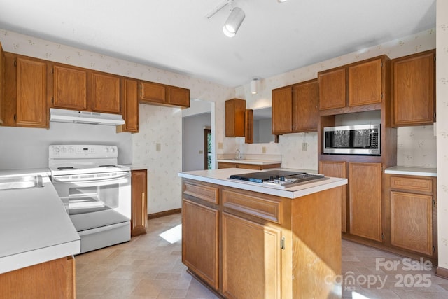 kitchen featuring under cabinet range hood, stainless steel appliances, light countertops, a center island, and wallpapered walls