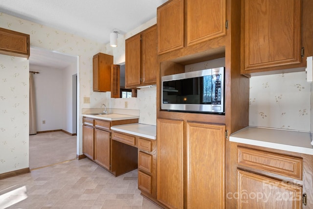 kitchen featuring wallpapered walls, stainless steel microwave, light countertops, and brown cabinetry