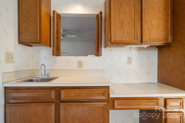 kitchen featuring a sink, a ceiling fan, light countertops, brown cabinets, and wallpapered walls