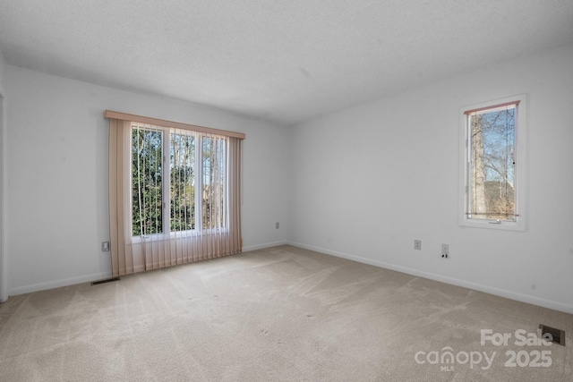 carpeted spare room with a textured ceiling, visible vents, and baseboards