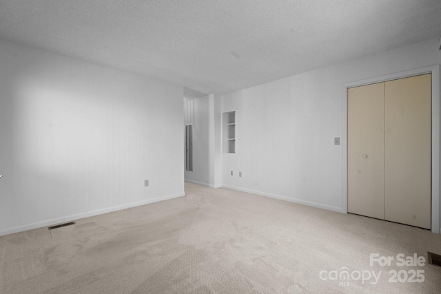 spare room featuring a textured ceiling, light carpet, visible vents, and baseboards