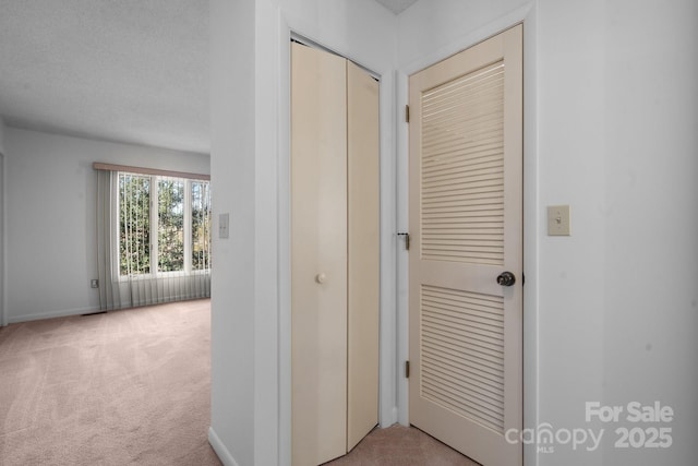 corridor with light carpet, a textured ceiling, and baseboards