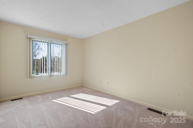 spare room with light colored carpet, visible vents, a textured ceiling, and baseboards